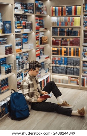 A studious young man engrossed in a book, seated on the floor of a bookshop.