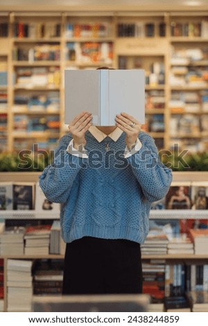 An unidentifiable person holding a book in front of face in a library. Royalty-Free Stock Photo #2438244859