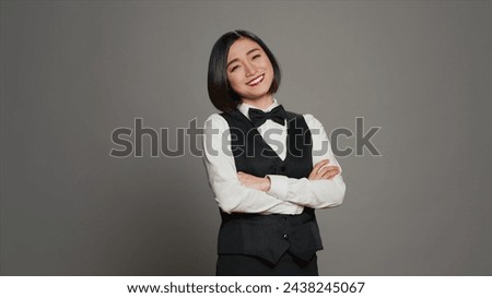 Asian receptionist posing with arms crossed on camera, feeling confident and professional in a formal suit and tie. Woman with front desk staff occupation, greeting guests in studio. Camera A.