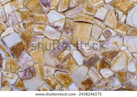 A wall made of stone with a pattern of brown and white stones. The wall is textured and has a rustic feel