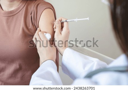 People getting a vaccination to prevent pandemic concept. Woman in medical face mask  receiving a dose of immunization coronavirus vaccine from a nurse at the medical center hospital Royalty-Free Stock Photo #2438263701