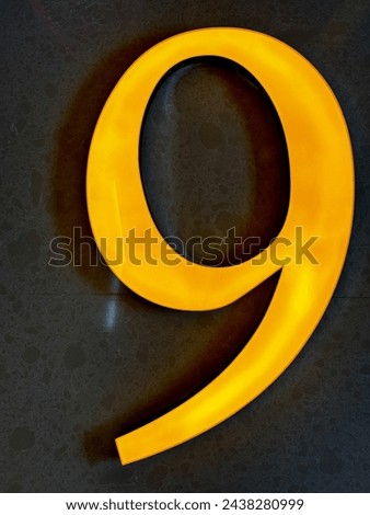 A large, illuminated number nine is displayed on a dark background. The number is surrounded by a yellow glow, making it stand out against the black background