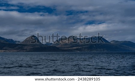 A picturesque mountain range of the Andes against a background of blue sky and clouds. View from the Beagle Canal. Ripples on the water. Argentina. Tierra del Fuego Archipelago