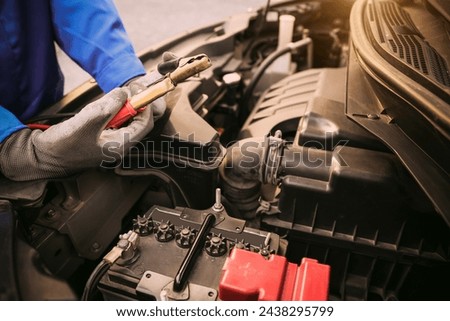 Close-up hand auto mechanic using connect jumper cable on terminal dead battery for jump-start or check car battery fail problem to change repairing and fix car and maintenance servicing. Royalty-Free Stock Photo #2438295799