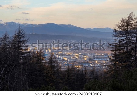 View from the mountain to the city of Magadan. Northern city among the mountains. Autumn season. Sunset. Larch trees in the foreground. Beautiful nature of the Russian Far East. Magadan region. Russia Royalty-Free Stock Photo #2438313187