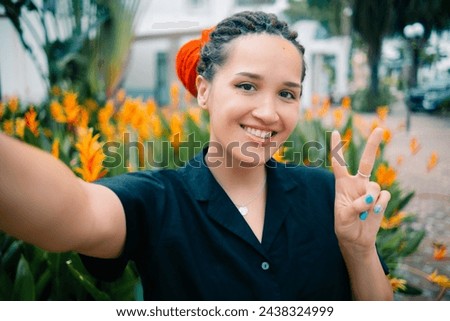 Young caucasian pretty woman with red dreadlocks showing heart sign, making selfie with happy smile on background exotic plants. High quality photo
