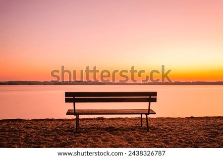 A lone bench offers a peaceful view across a calm lake beneath a colorful, dusky sky, reflecting the serene ambiance of a Swedish evening. Royalty-Free Stock Photo #2438326787