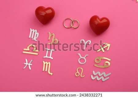 Zodiac compatibility. Signs, wedding rings and red hearts on pink background, flat lay Royalty-Free Stock Photo #2438332271