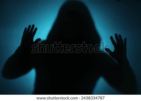 Silhouette of ghost behind glass against blue background