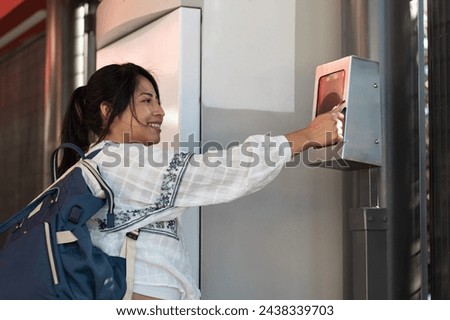 photograph with copy space of a brown skin tourist woman, traveling alone in her 20s, paying for her access to the transportation service, at the check-in machine, with her card, at the bus station