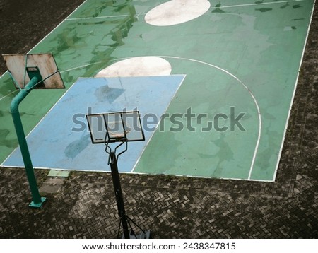 The green basketball court partially gets wet after the rain. In the middle of the paving block area. Permanent and mobile basket board. Top view