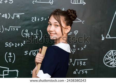 A schoolgirl girl with books and textbooks in her hands, teenage girl 10-12 years old in a school class. Royalty-Free Stock Photo #2438380243