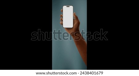 Black African-American hand displays a modern smartphone with a blank screen against a deep teal background, ideal for presenting apps or mobile interfaces in a clean and contemporary setting Royalty-Free Stock Photo #2438401679