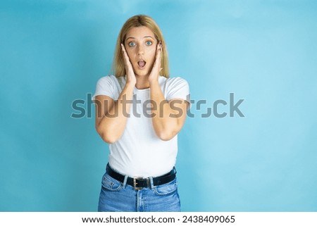Young beautiful woman wearing casual t-shirt over isolated blue background screaming and surprised with her hands around her mouth