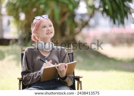 Young Happy Artist woman drawing book and wearing headphones in the garden.