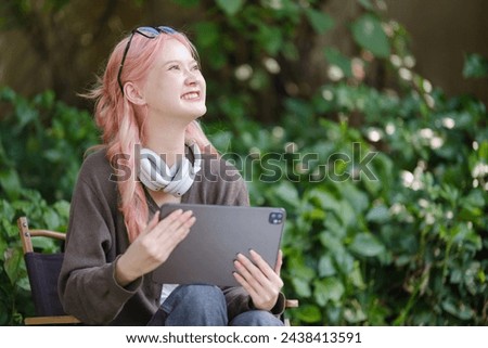 A cute pink-haired girl drawing on a digital tablet and wearing headphones in the garden, a Woman Doing Freelance Work in the Garden, and a woman with a digital tablet with artwork.