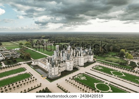 A sprawling castle, Chateau de Chambord, stands out in a vast park. Its grand architecture and lush surroundings create a stunning aerial view of history and nature blending seamlessly