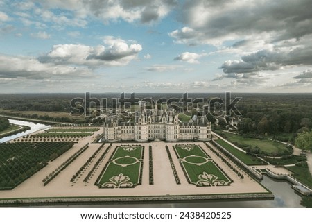 An aerial view of the magnificent Chateau de Chambord standing proudly amidst a dense forest of towering trees, creating a stunning contrast between man-made architecture and natural surroundings