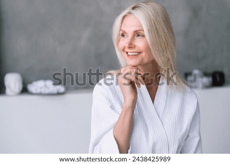 Headshot of happy middle aged woman in white bathrobe looking away, standing in bathroom. Female spending weekend morning at spa hotel. Advertising antiage, recreation, skincare, bodycare procedures Royalty-Free Stock Photo #2438425989