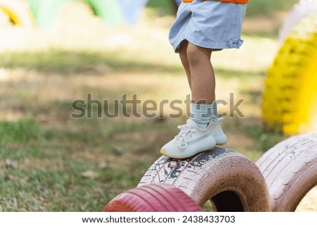 A child is standing on a tire in a park. The tire is surrounded by other tires, creating a fun and playful atmosphere Royalty-Free Stock Photo #2438433703