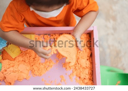 A child girl is playing with sand in a tray
