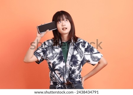 HAPPY SONGKRAN DAY. Cheerful lovely young asian woman in summer clothing with gesture of hand Holding mobile phone isolated on orange background. Songkran festival. Thai New Year's Day. Royalty-Free Stock Photo #2438434791