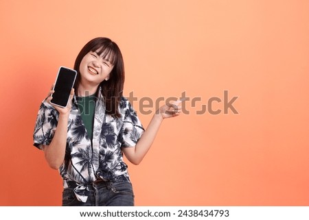 HAPPY SONGKRAN DAY. Cheerful lovely young asian woman in summer clothing with gesture of hand Holding mobile phone isolated on orange background. Songkran festival. Thai New Year's Day. Royalty-Free Stock Photo #2438434793
