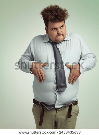 Man, stomach and plus size with belly from unhealthy diet or weight gain on a studio background. Young male person or big guy holding tummy for eating disorder or body conscious on mockup space Royalty-Free Stock Photo #2438435633