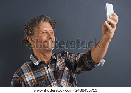 Mature, man and happy selfie in studio and learning about photography on dark background. Filming, video or click record for profile picture and post online to social media with website or blog