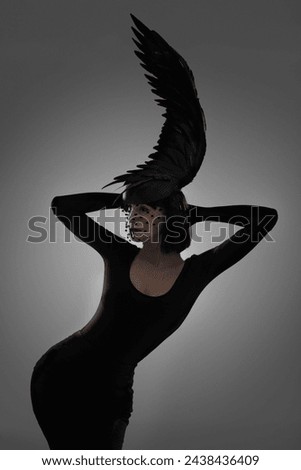 Bird, fashion and art style woman in a studio with head piece, feather hat and abstract with unique creativity. Crow, silhouette and shadow with fantasy and with goth clothes and grey background