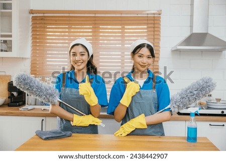 Cleaning service women in uniform stand on kitchen counter holding duster foggy spray and rag. Emphasizing teamwork in efficient housework. Clean portrait two uniform maid working smiling employee. Royalty-Free Stock Photo #2438442907
