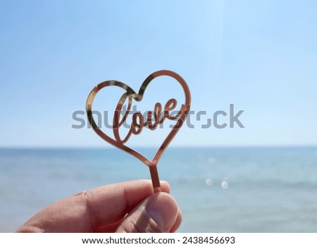 Person holding in fingers hand stick in shape heart and words Love you on background sea and sea waves, blue sky in seashore on sunny summer day close-up. Concept love romance amour St Valentines Day