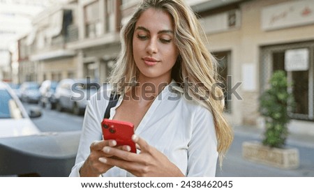 Attractive young blonde woman seriously engrossed in her cellphone, standing coolly on a sunny, urban street, with a relaxed concentration that's all about today's digital lifestyle. Royalty-Free Stock Photo #2438462045