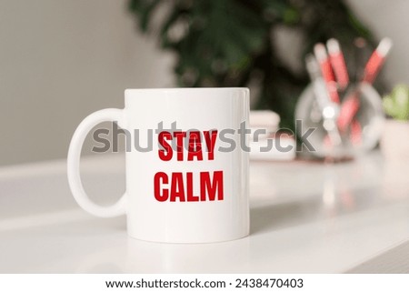 Coffee mug with text - STAY CALM in workplace background.