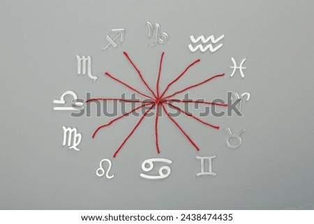 Zodiac compatibility. Signs and red threads on grey background, flat lay Royalty-Free Stock Photo #2438474435