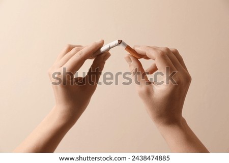 Stop smoking. Woman holding broken cigarette on beige background, closeup Royalty-Free Stock Photo #2438474885
