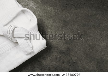 White karate belt and kimono on gray textured background, top view. Space for text Royalty-Free Stock Photo #2438480799