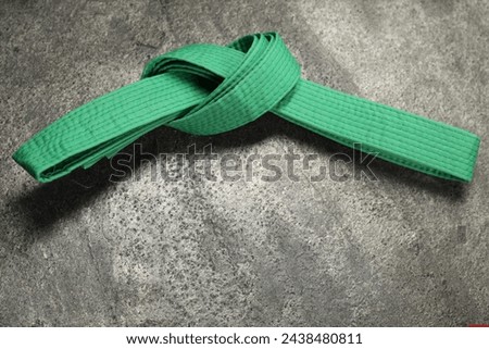 Green karate belt on gray textured background, top view. Space for text Royalty-Free Stock Photo #2438480811