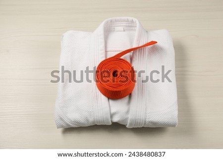 Orange karate belt and white kimono on wooden background, top view Royalty-Free Stock Photo #2438480837