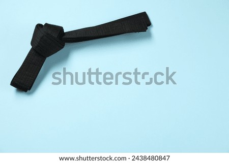 Black karate belt on light blue background, top view. Space for text Royalty-Free Stock Photo #2438480847