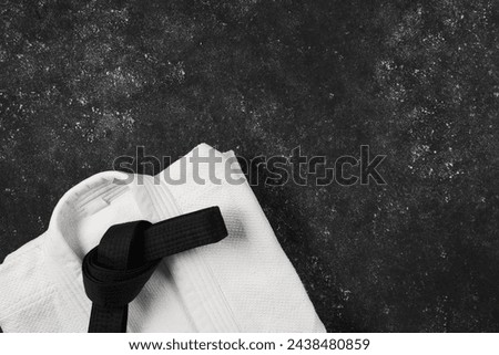 Black karate belt and white kimono on gray textured background, top view. Space for text Royalty-Free Stock Photo #2438480859