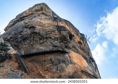 Tourists prepare to ascend the top of Sigiriya Rock, holding onto the railing, with a panoramic view of the site. Dambulla, Sri Lanka.