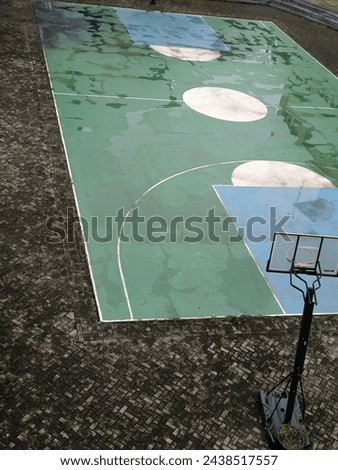 The green basketball court gets wet after the rain. In the middle of the paving block area. Top view