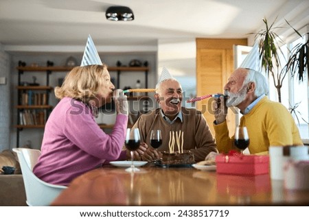 Group of happy senior friends having fun with party horn blowers on a Birthday party at home.