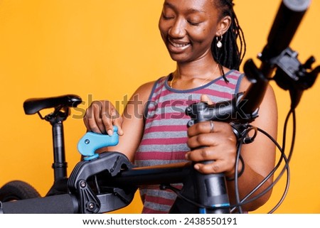 Detailed view of black woman examining damaged bike frame on repair stand against yellow background. African american lady securing and making necessary adjustments on modern bicycle. Royalty-Free Stock Photo #2438550191