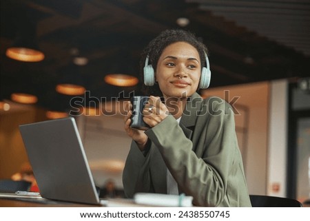 A woman with headphones at a table with a laptop and coffee in nice modern coworking office