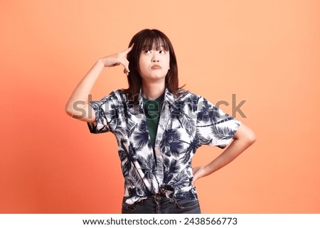 HAPPY SONGKRAN DAY. Cheerful lovely young asian woman in summer clothing with gesture of thinking isolated on orange background. Thai New Year's Day. Royalty-Free Stock Photo #2438566773