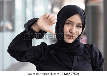 Smiling Muslim Woman Expressing Disagreement with thumb down hand Gesture, concept image of Wrong, Rejection, no way, no, bad, deny, refuse, disagree, dislike, Unhappy and Negative expression
