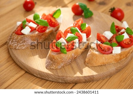 Bruschetta with cherry tomatoes, mozzarella cheese and basil in sun rays on wooden board. Traditional Italian appetizer, snack or antipasto. Vegetarian food. Healthy eating. Mediterranean food. Royalty-Free Stock Photo #2438601411
