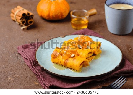 Thin pumpkin pancakes rolled into a roll and topped with honey and jam on a gray ceramic plate on a brown concrete background. Pancake recipes. International Pancake Day. Maslenitsa, carnival